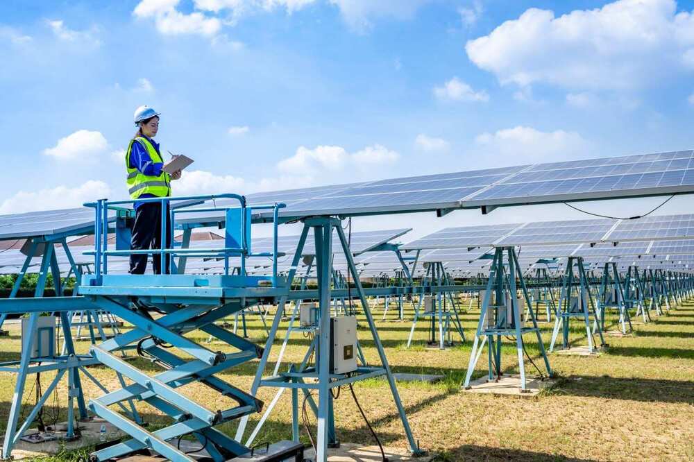 Femme sur une nacelle élevatrice à côté d'une centrale au sol prenant des notes en rapport avec le PPE3